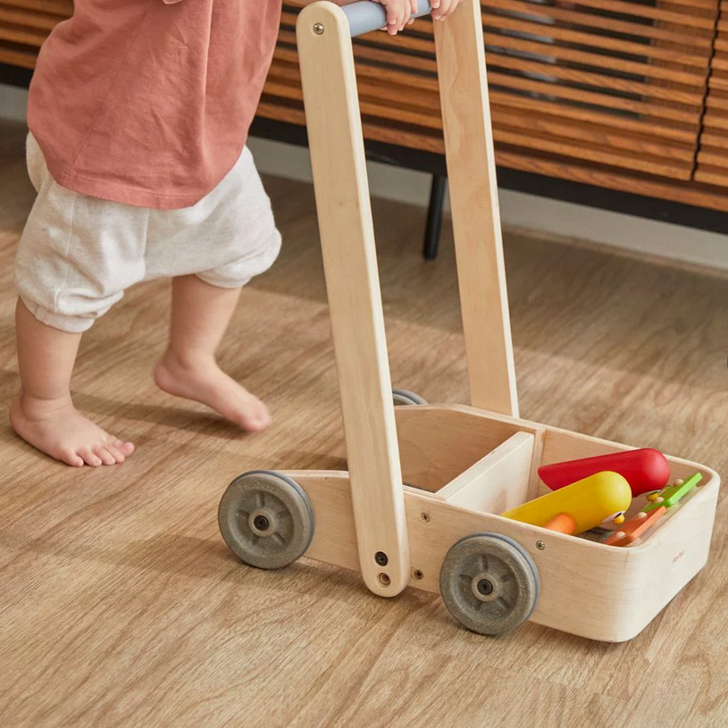 Child playing with a wooden toy cart on a wooden floor