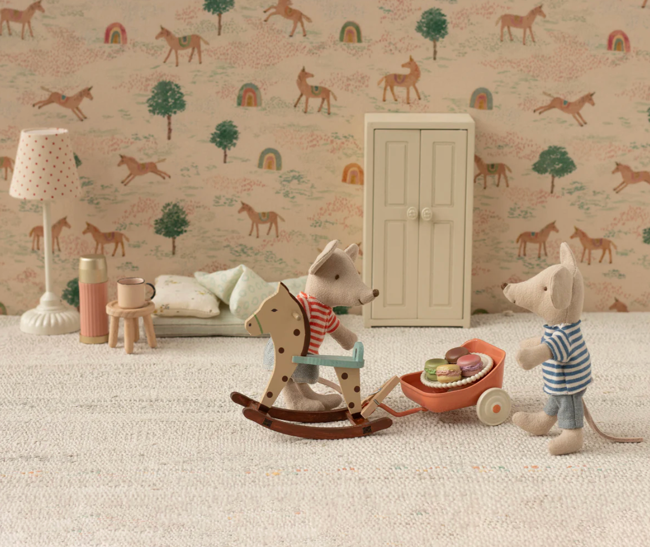 Children's room with toys, a rocking horse, and a cabinet against a wallpapered wall.