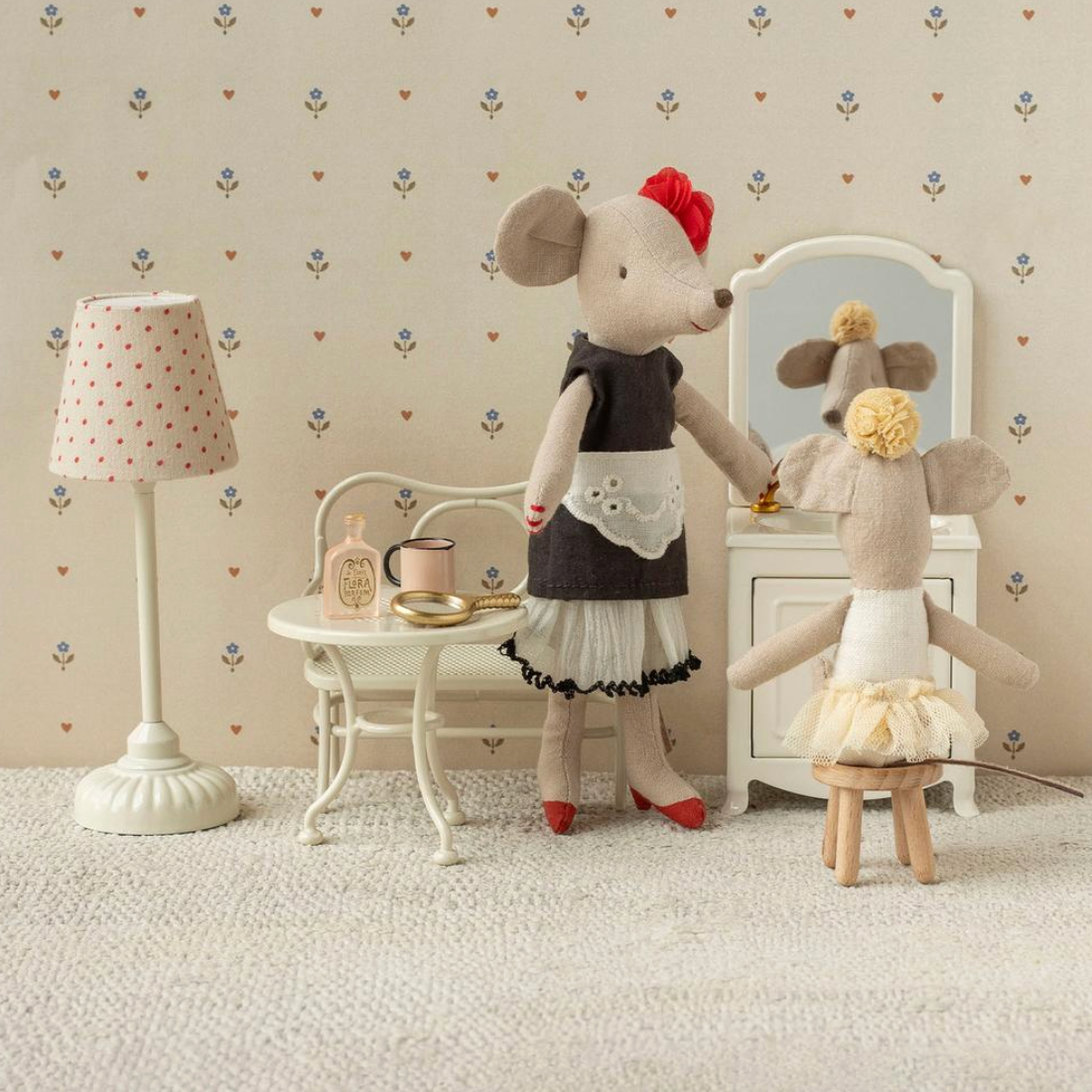 Two mouse dolls in a room with a lamp, table, and mirror on a patterned wallpaper background.