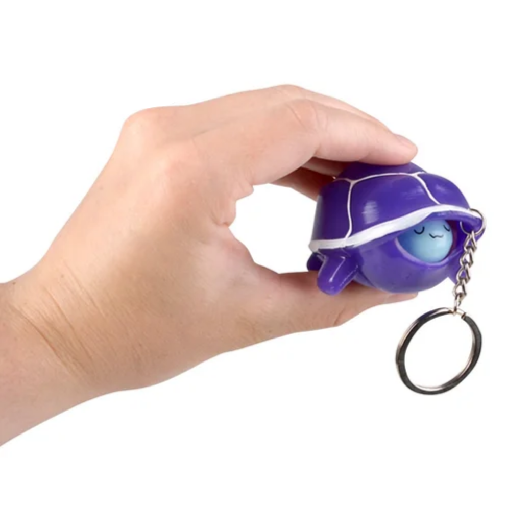 Hand holding a purple turtle-shaped keychain with a white background