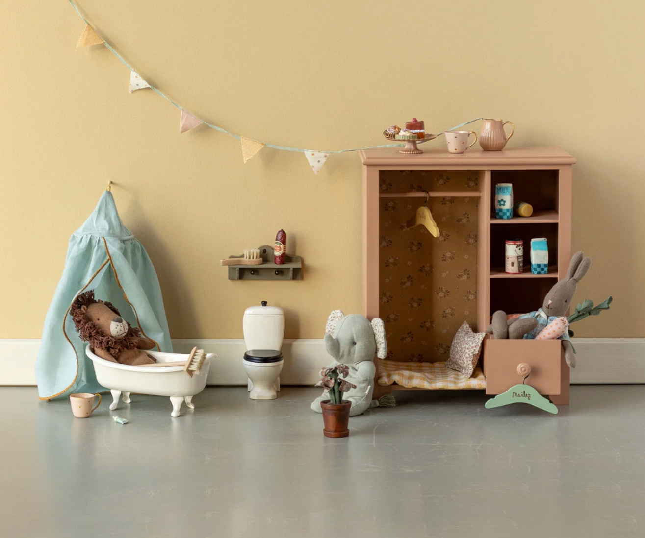 Children's playroom with toy bathtub, toilet, and furniture against a beige wall.
