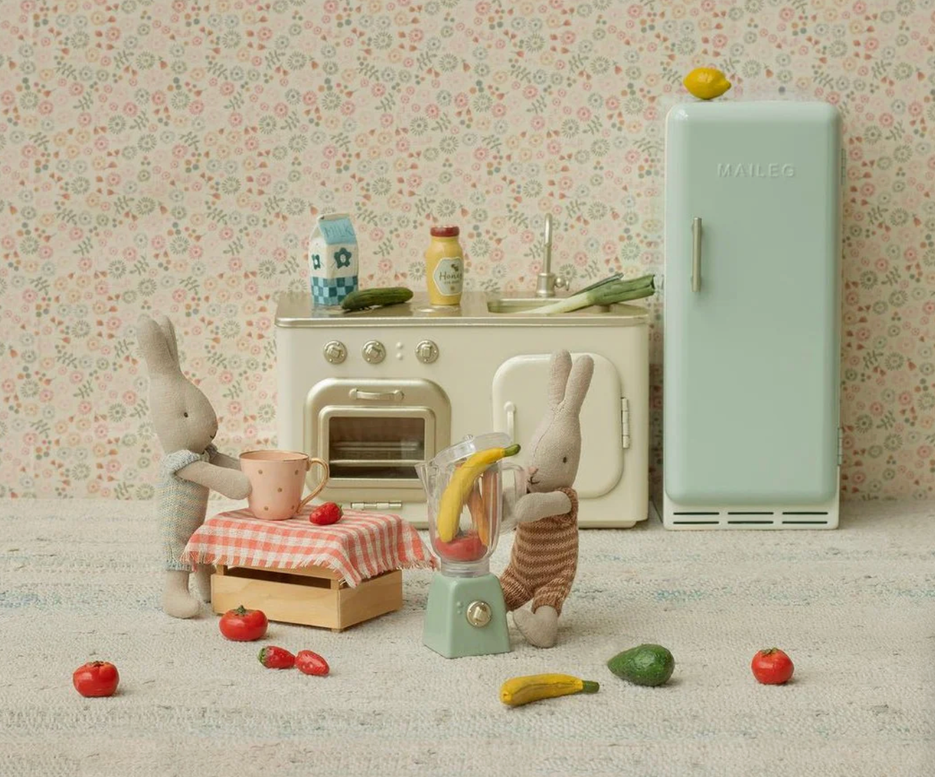 Miniature kitchen set with toy refrigerator, oven, and appliances on a floral wallpaper background.