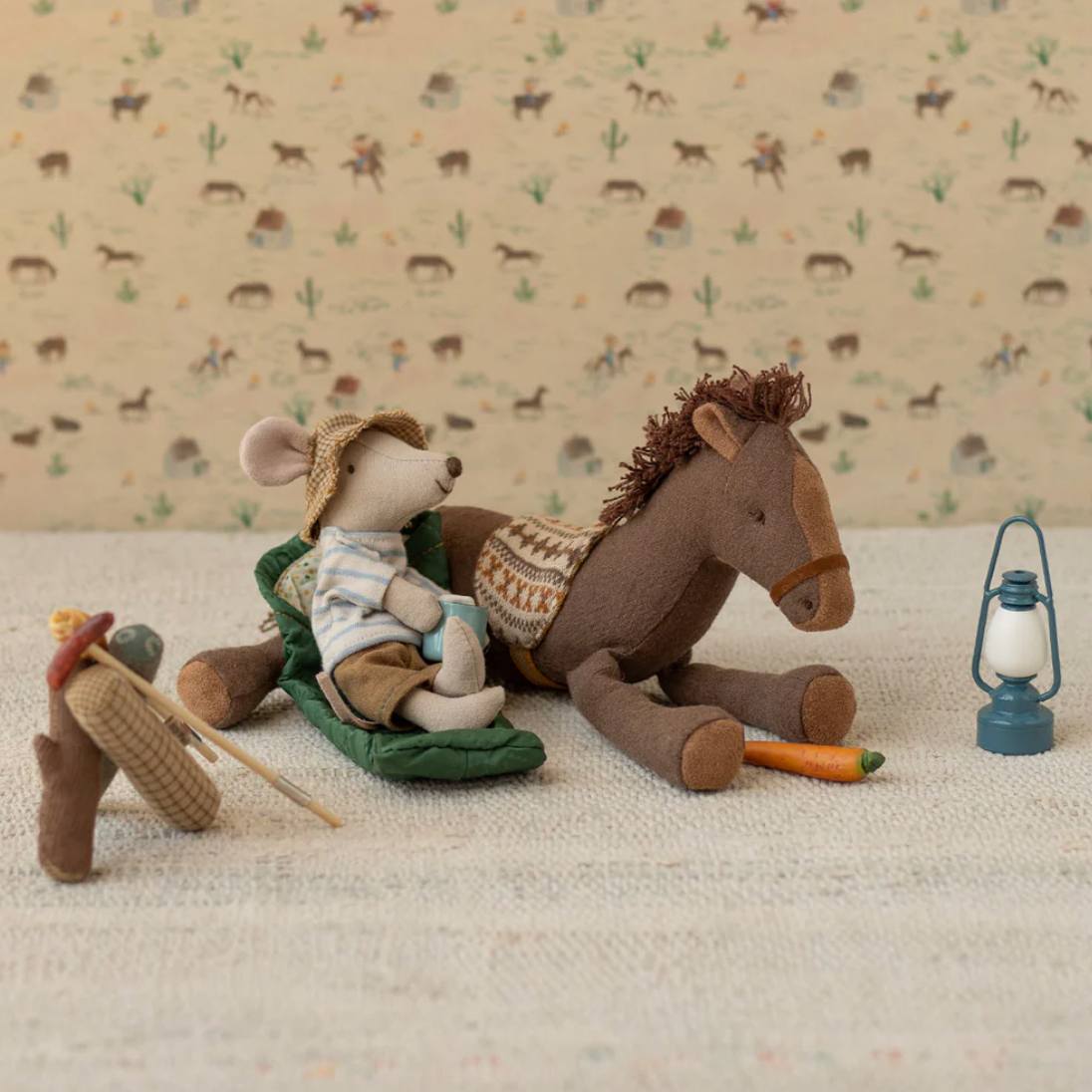 Stuffed mouse and horse with a lantern on a textured surface with animal patterned background