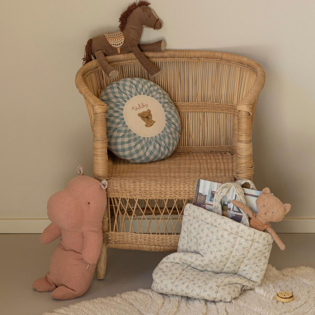 Wicker chair with teddy bear, plush toy, and decorative items against a beige wall.