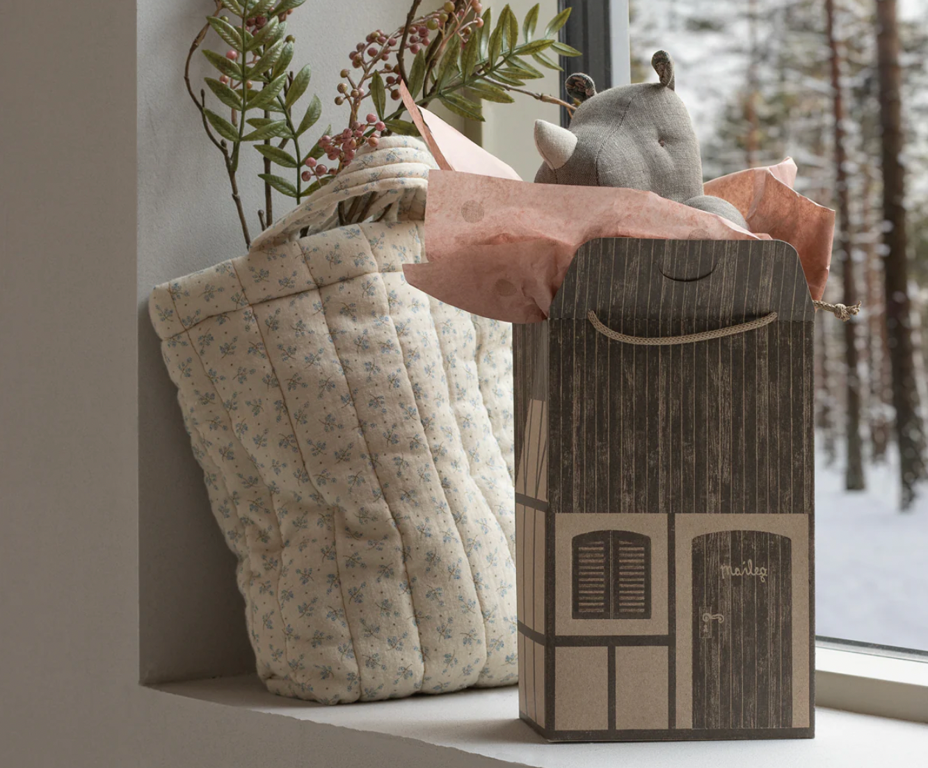 Decorative storage basket with a plush toy and floral arrangement on a windowsill.