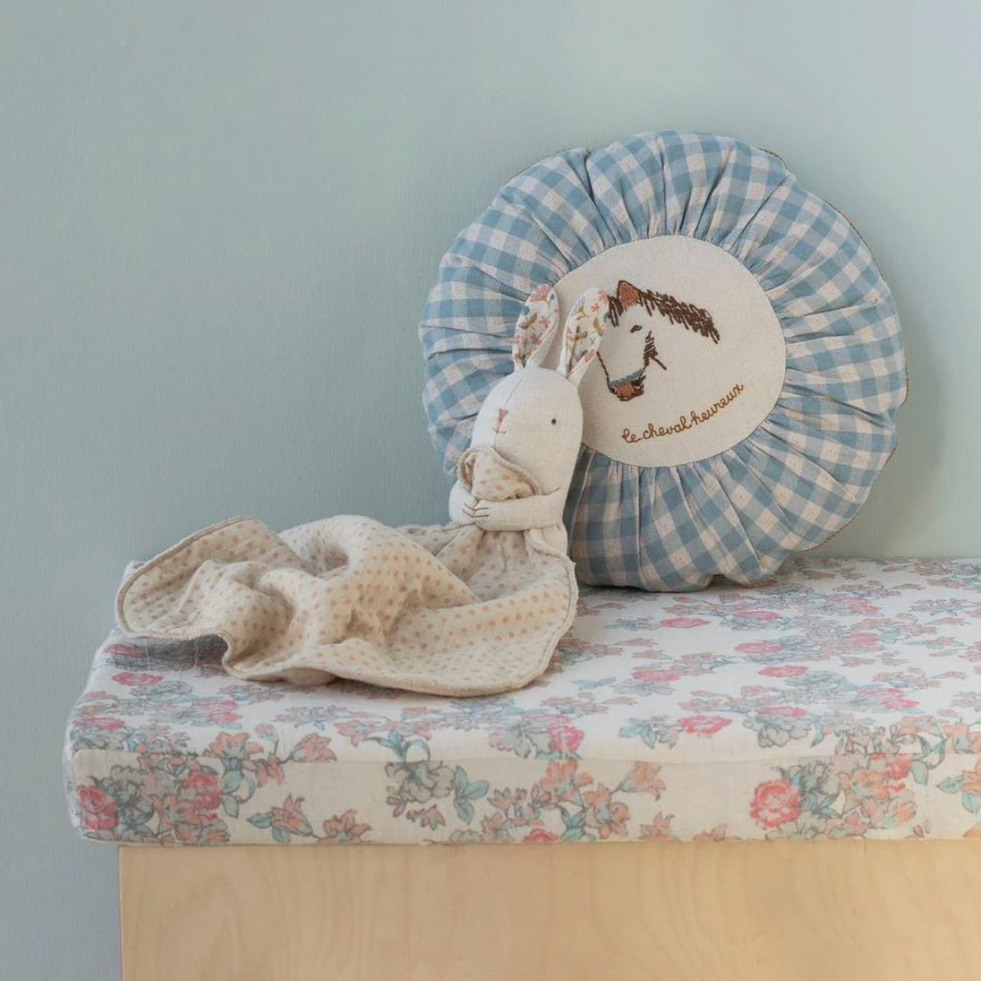 Decorative pillow with a horse design on a floral cushion against a light blue wall.