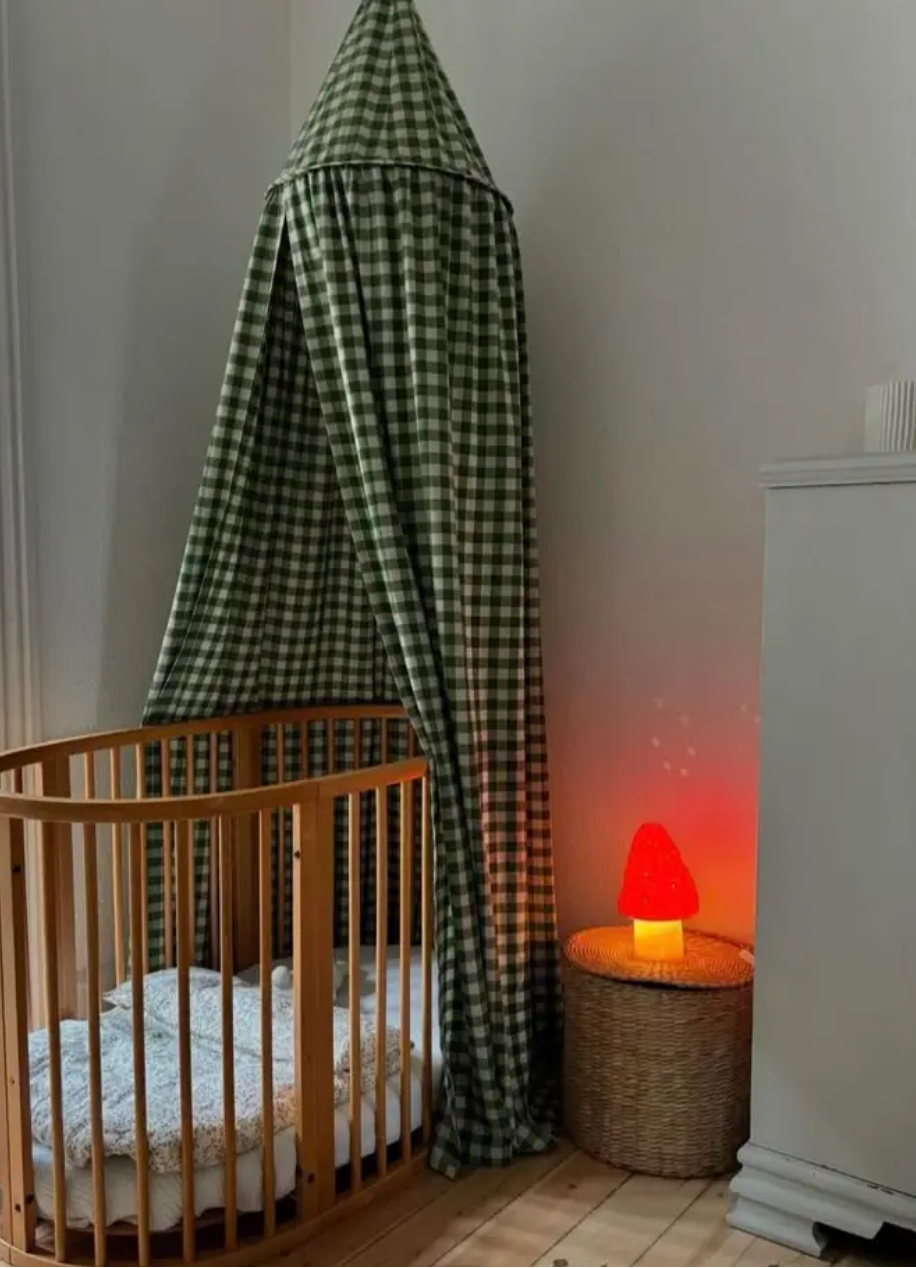 Wooden crib with green checkered canopy in a room with a red night light.