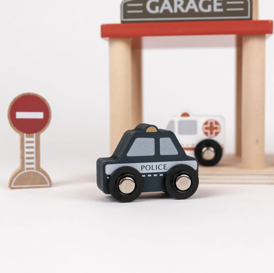 Toy police car with a wooden garage and ambulance in the background