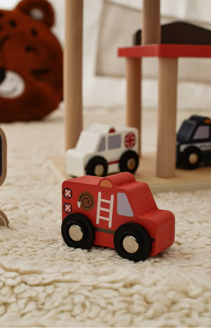 Red toy fire truck on a carpeted floor with other toys in the background