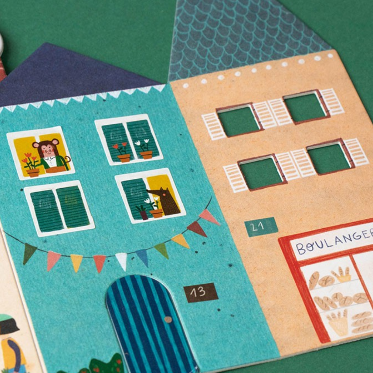 Illustrated paper houses with windows and a bakery sign on a green background