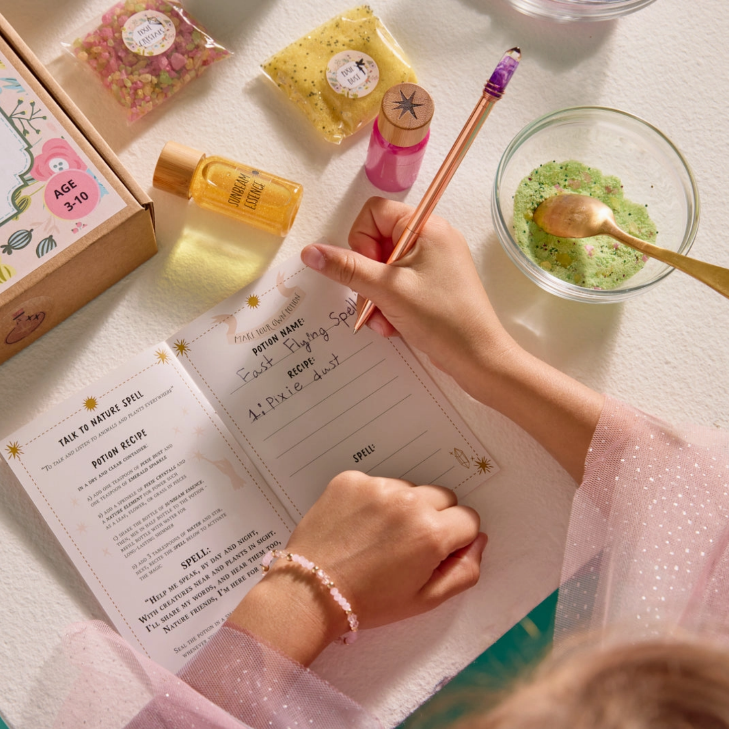 Person writing in a notebook with a box labeled 'Tale of Farland' and various items on a table.