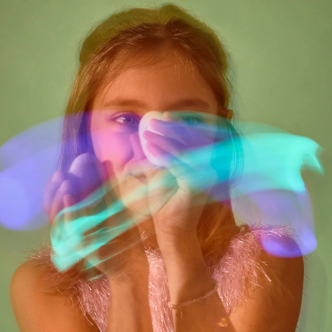 Person holding colorful, translucent gloves in front of their face against a light green background