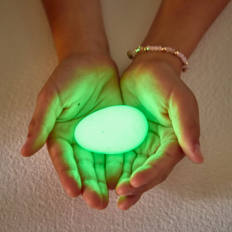 Hands holding a glowing green sphere against a neutral background