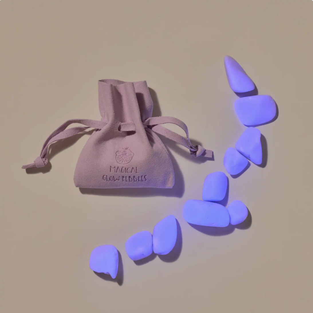 Purple glow-in-the-dark necklaces with a drawstring bag labeled 'Magical Glow Pebbles' on a beige background.