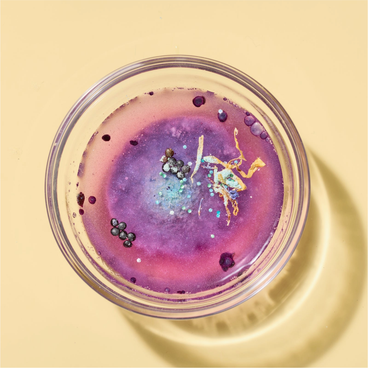 Glass container with colorful liquid and solid particles on a yellow background