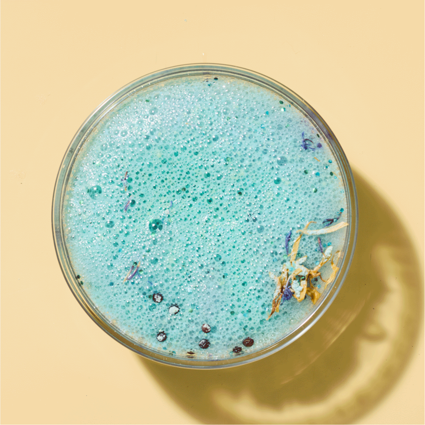 Bowl of blue bath bomb mixture with decorative elements on a beige background