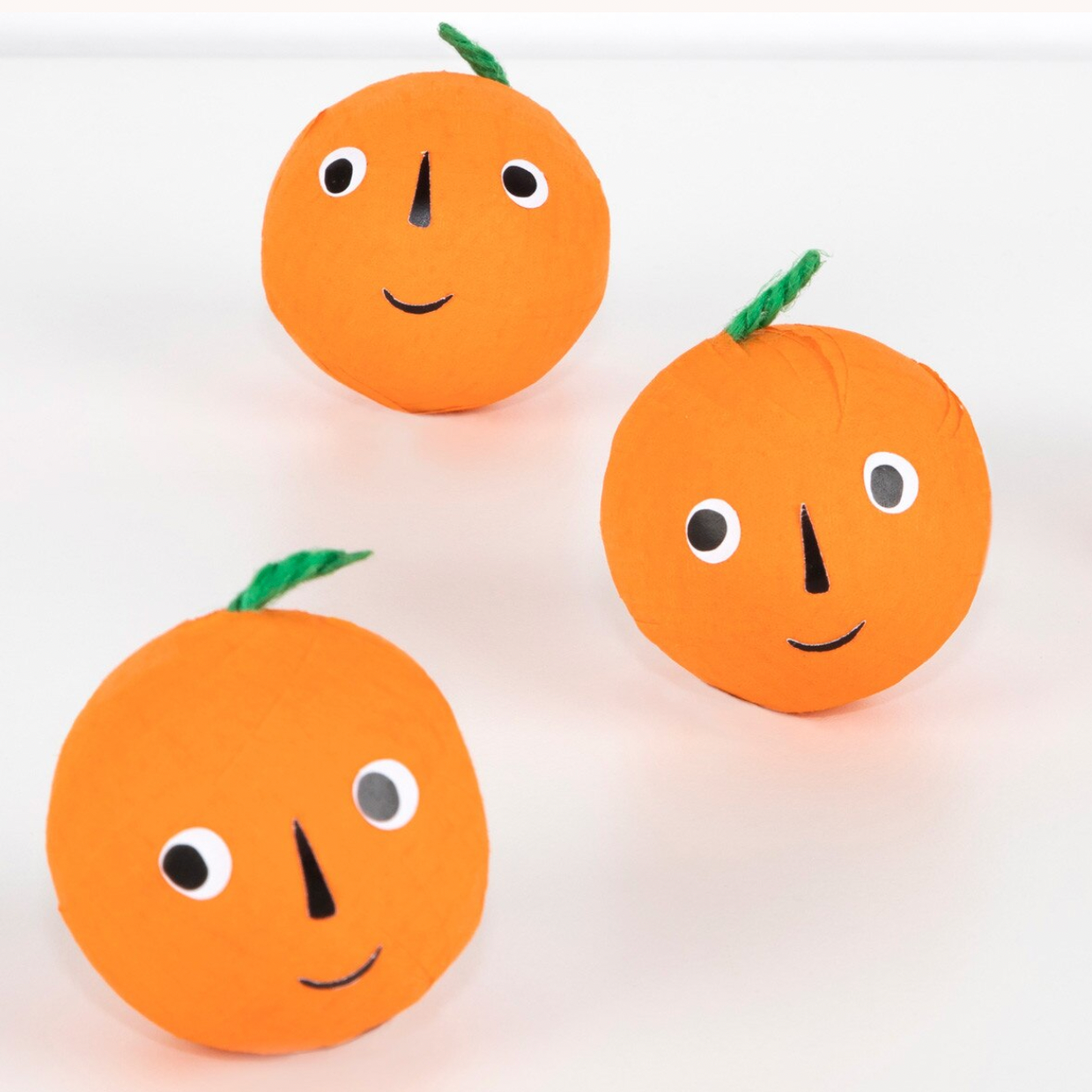 Three orange-shaped plush toys with handmade paper faces and green stems, arranged on a plain white background.