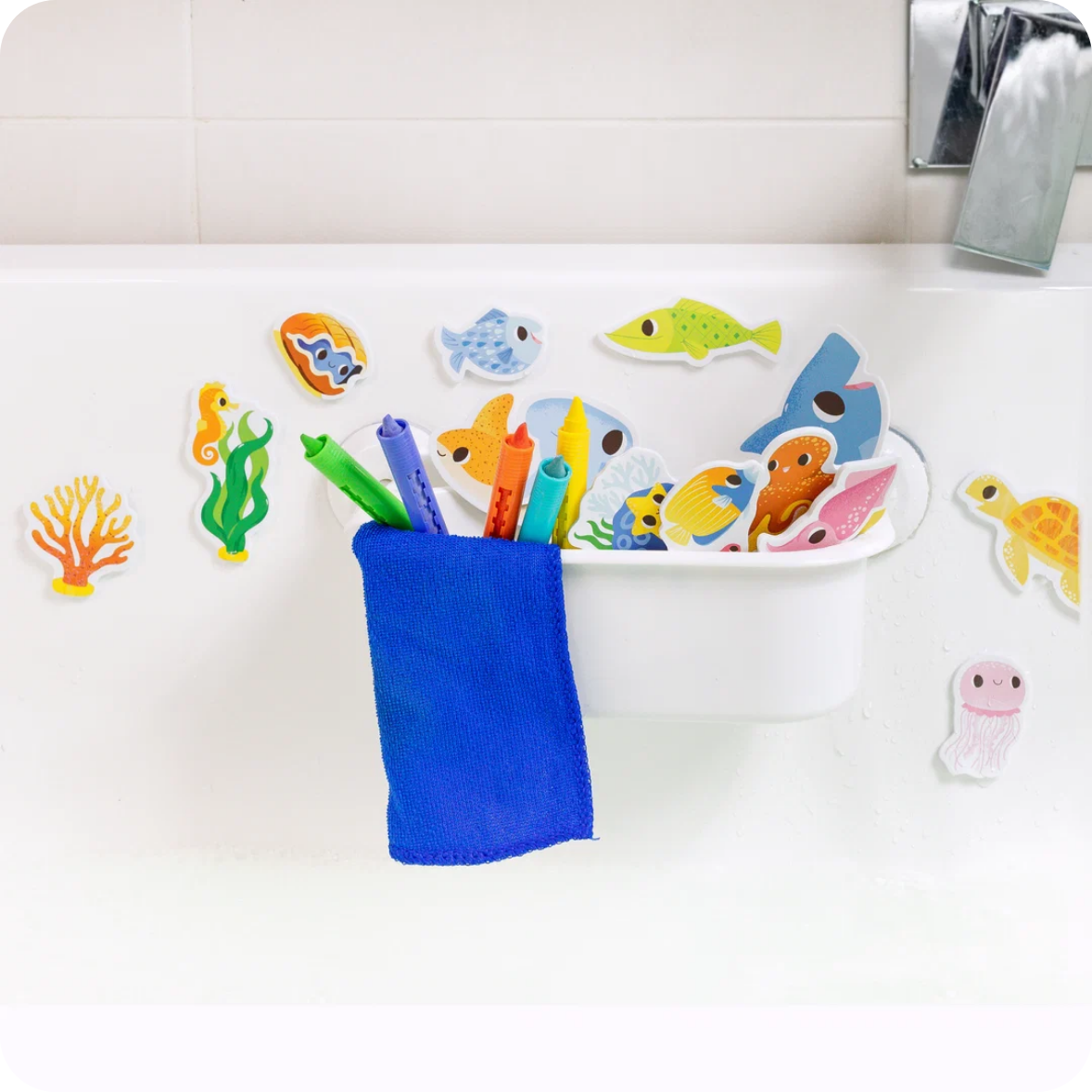 A white bathtub with colorful magnetic fish and sea life toys attached around it, plus a blue sponge holder with pens and a sponge resting in it. A chrome faucet is visible in the upper right.