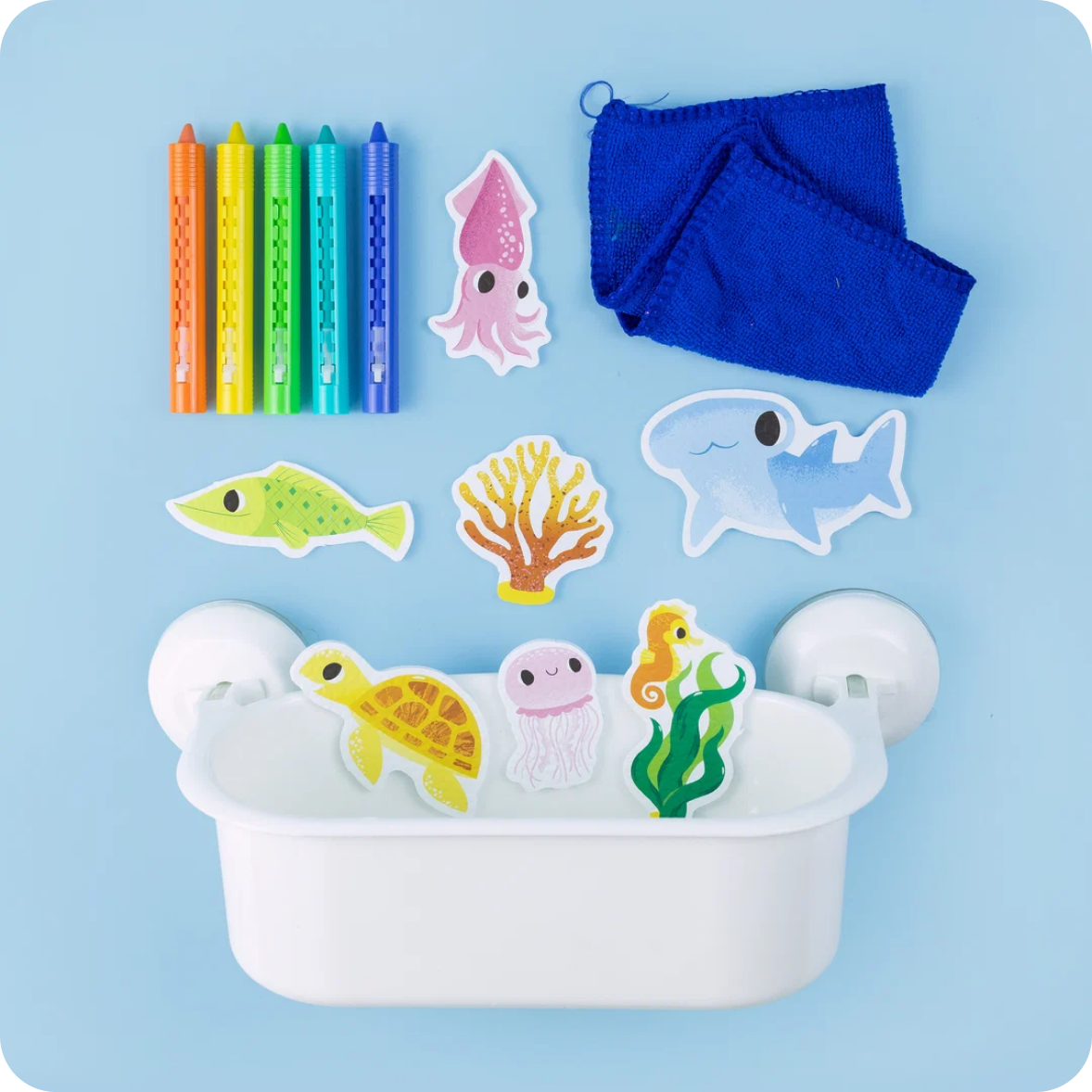 A bath toy set arranged on a light blue background, including six colorful crayons, a blue cloth, and several sea-themed cutout pieces such as a squid, fish, coral, shark, turtle, jellyfish, seahorse, and a white tub with suction cups.