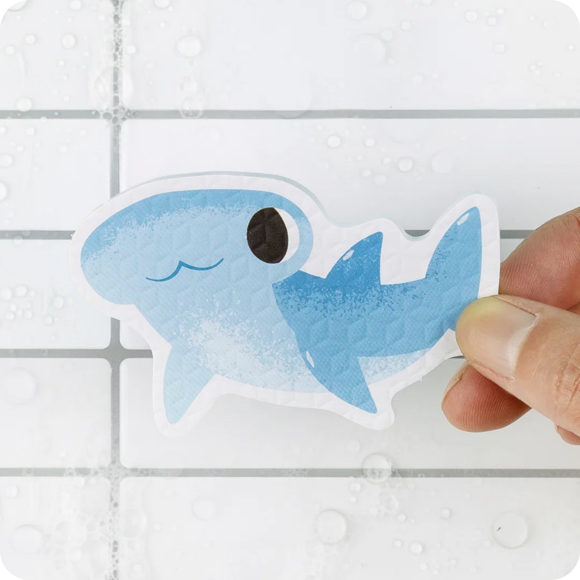 Hand holding a blue shark-shaped toy against a tiled bathroom background