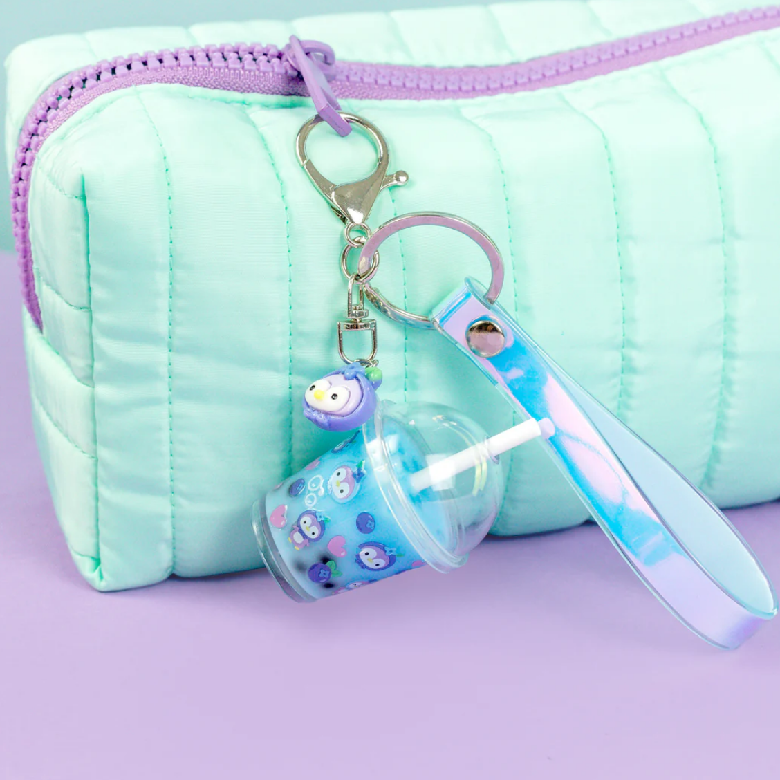 A mint green quilted zippered pouch with a lavender zipper, shown with a keychain charm featuring a small owl and a clear cup accessory on a lavender background.