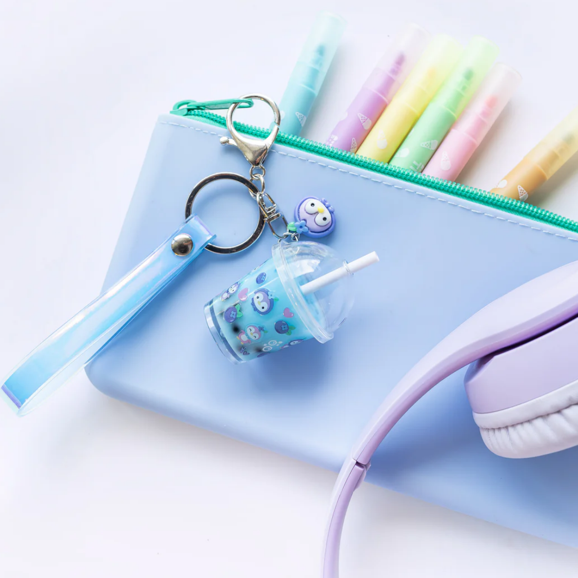 Pastel-colored pencil case with stationery items including a keychain and headphones on a light blue background.