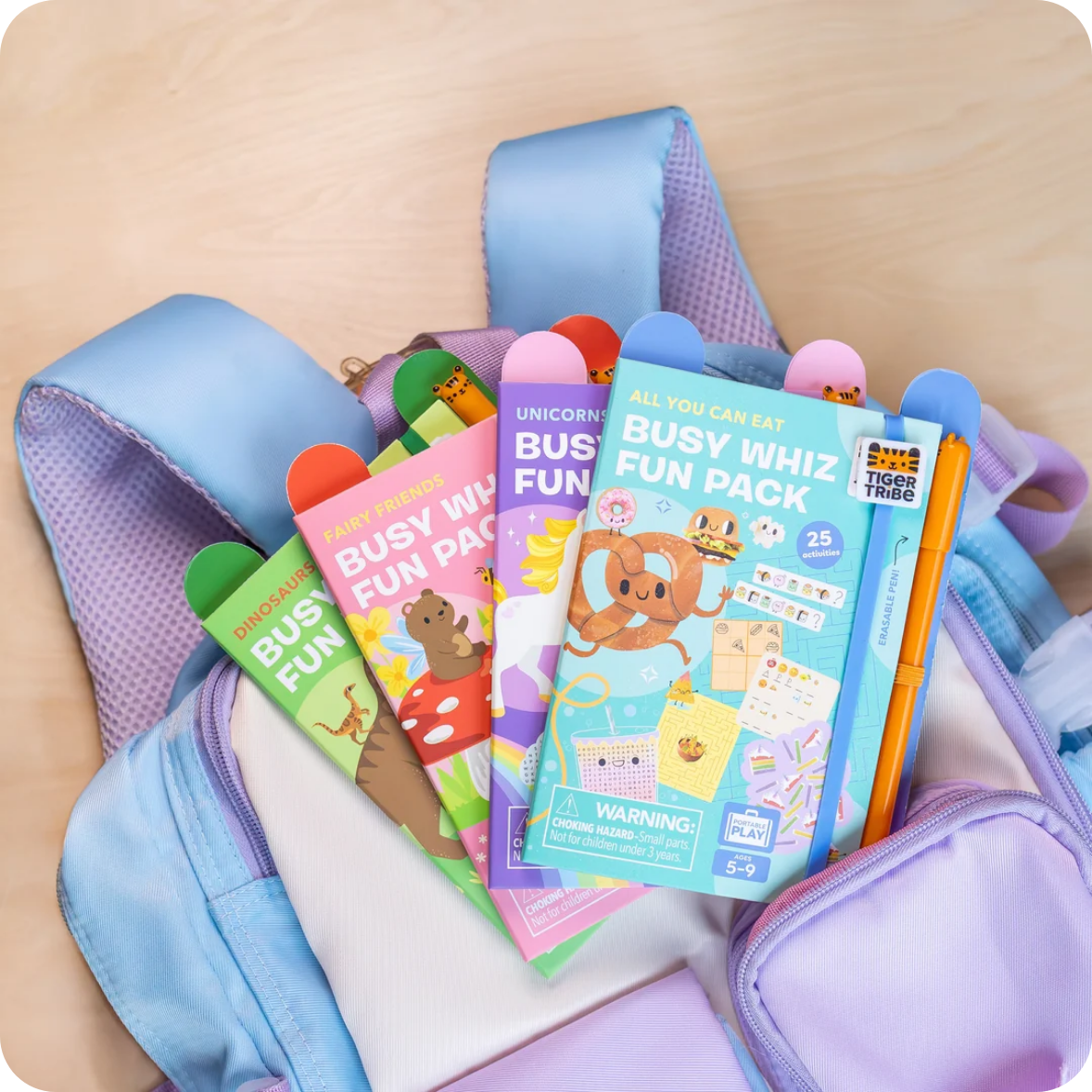 Colorful children's activity packs with a pencil in a blue and purple bag on a beige surface