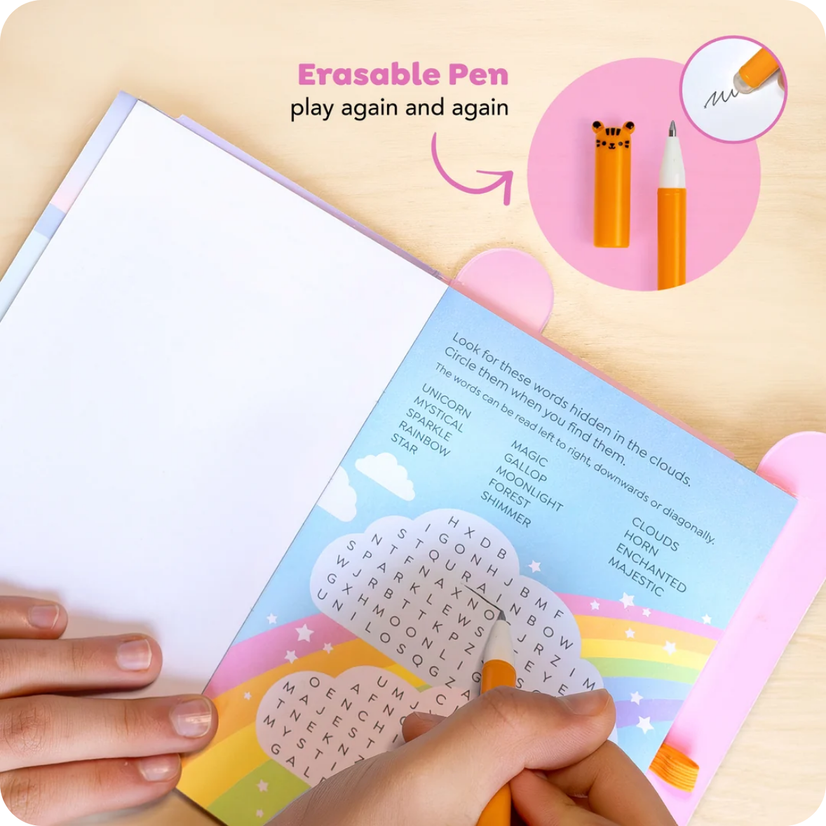 A children's word-search activity book being held on a light wood surface, with a hand using an orange erasable pen. The cover shows colorful rainbow, cloud, and star graphics, and the top of the page has text reading 'Erasable Pen play again and again.