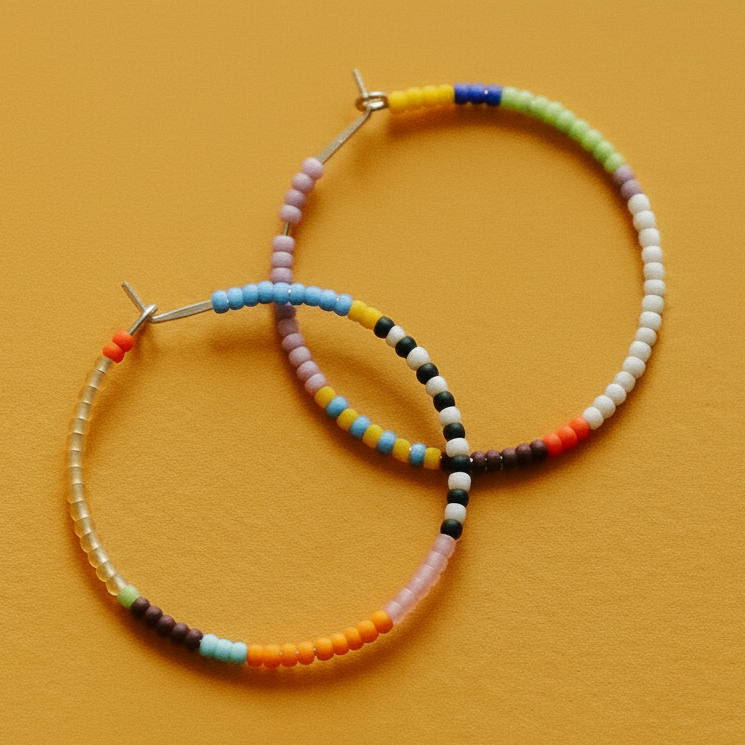 Handmade hoop earrings made of small multicolored seed beads, displayed on a textured mustard yellow background.
