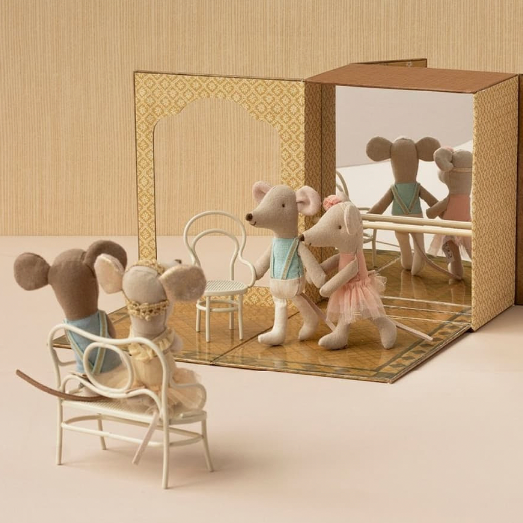 A miniature dollhouse-style scene with small mouse figures posed inside and around a folding stage set. The stage has patterned panels, a mirror, and a wooden floor, with small furniture pieces including chairs and a table.