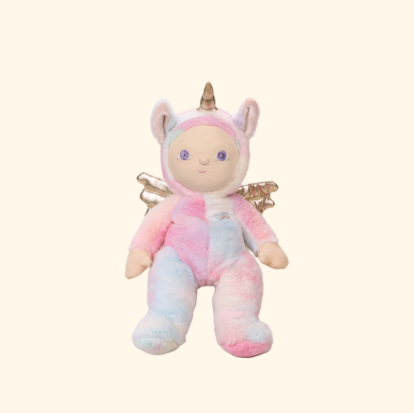 A plush unicorn toy with pastel pink, blue, and white tie-dye coloring, featuring a gold horn, small wings, and a pale face, centered on a solid cream background.