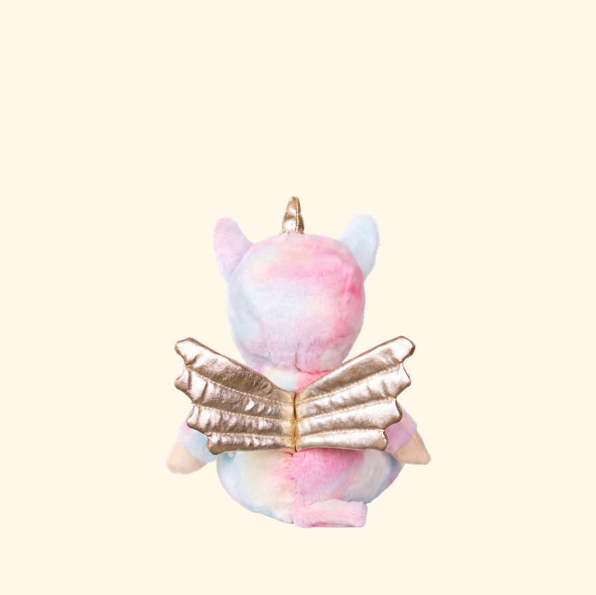 A pastel pink, blue, and white plush unicorn keychain or bag charm shown from the back, featuring metallic gold wings and a gold hanging loop, set against a solid cream background.