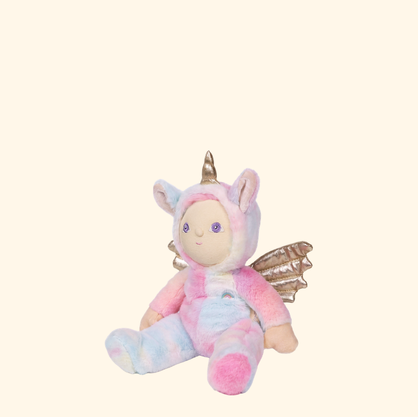 A plush unicorn doll wearing a pastel tie-dye hooded outfit in pink, blue, and white, with a gold horn, embroidered face, and metallic gold wings, seated against a solid pale cream background.