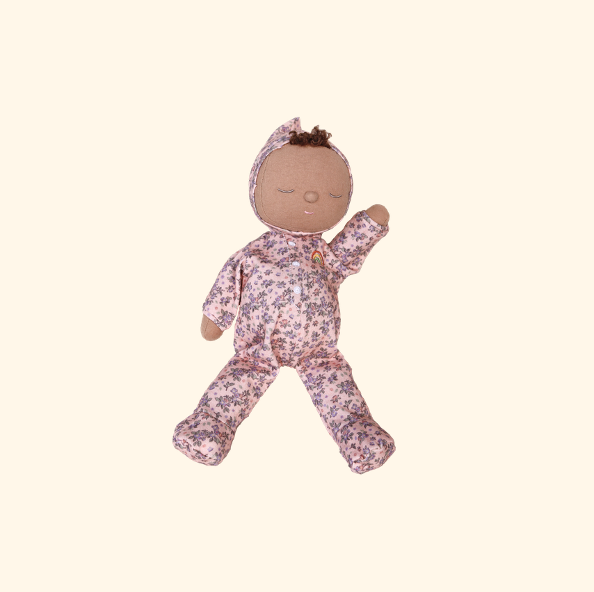 A handmade fabric doll with a brown face and hands, wearing a pink floral pajama set with a matching bonnet, isolated on a light cream background.