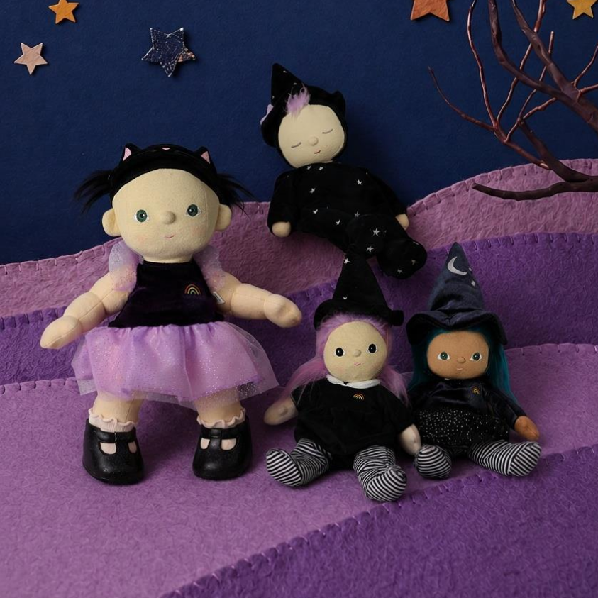 Four witch-themed plush dolls arranged on purple steps against a dark blue fabric sky backdrop with a gold crescent moon, stars, and bare branches.