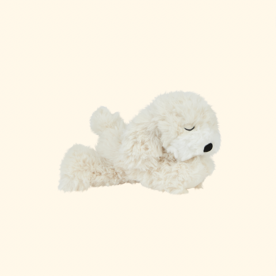 A fluffy white dog-shaped plush toy with closed eyes and a small black nose, lying on a plain warm cream background.