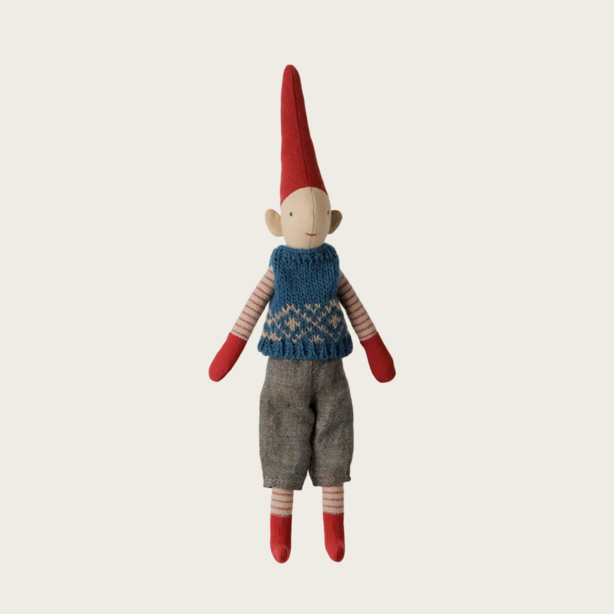 A handmade blue knit Christmas gnome doll. The doll features a tall red hat, a blue knit vest, striped red and beige sleeves, and gray pants.