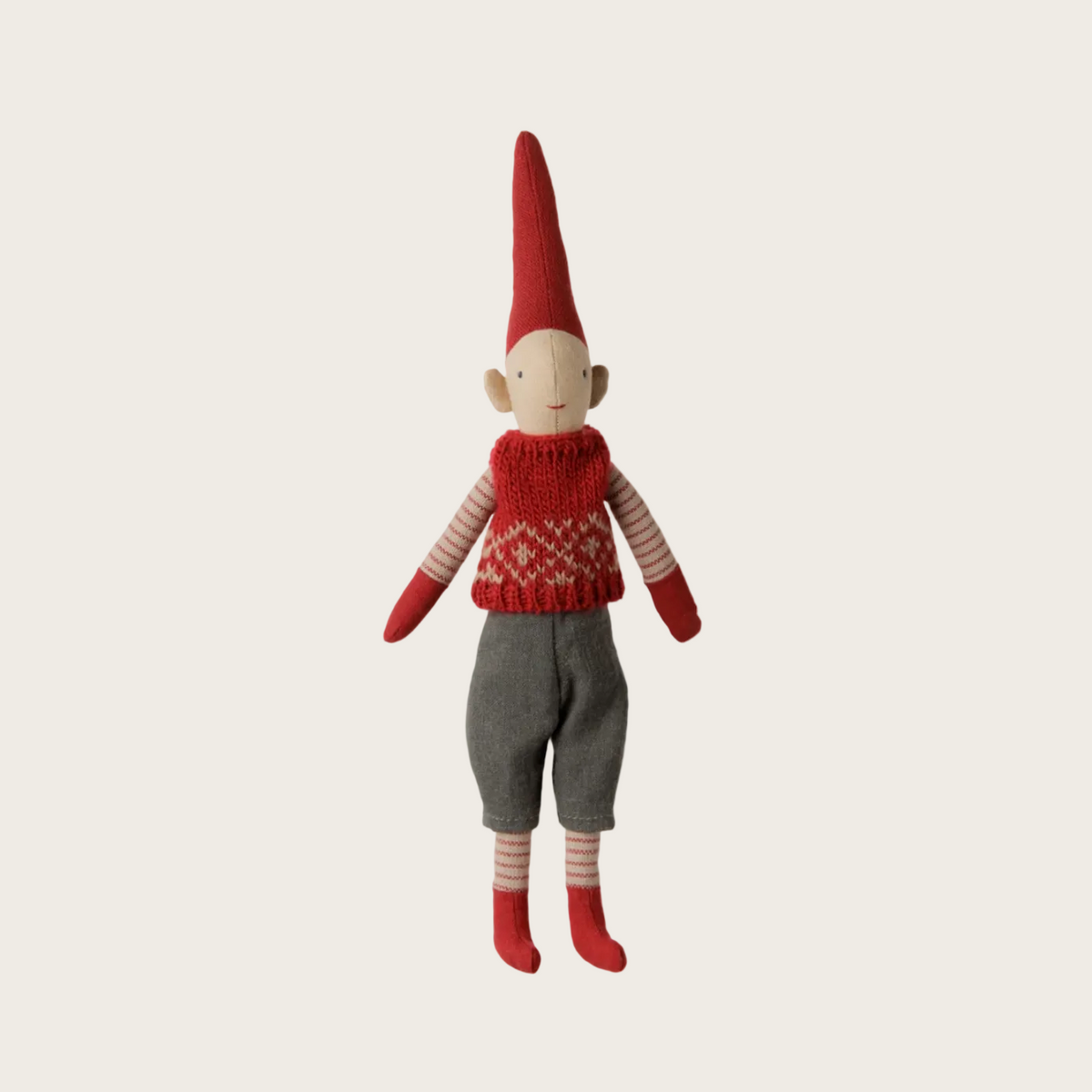 A handmade doll or gnome figure with a tall red pointed hat, red knit sweater, gray pants, and red striped socks, shown on a light beige background.