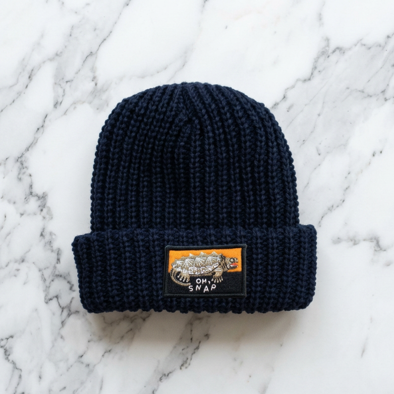 A navy blue knit beanie with a rectangular embroidered patch on the front, shown against a white textured background. The patch features a tiger and the text 'OH MY SHAR'.