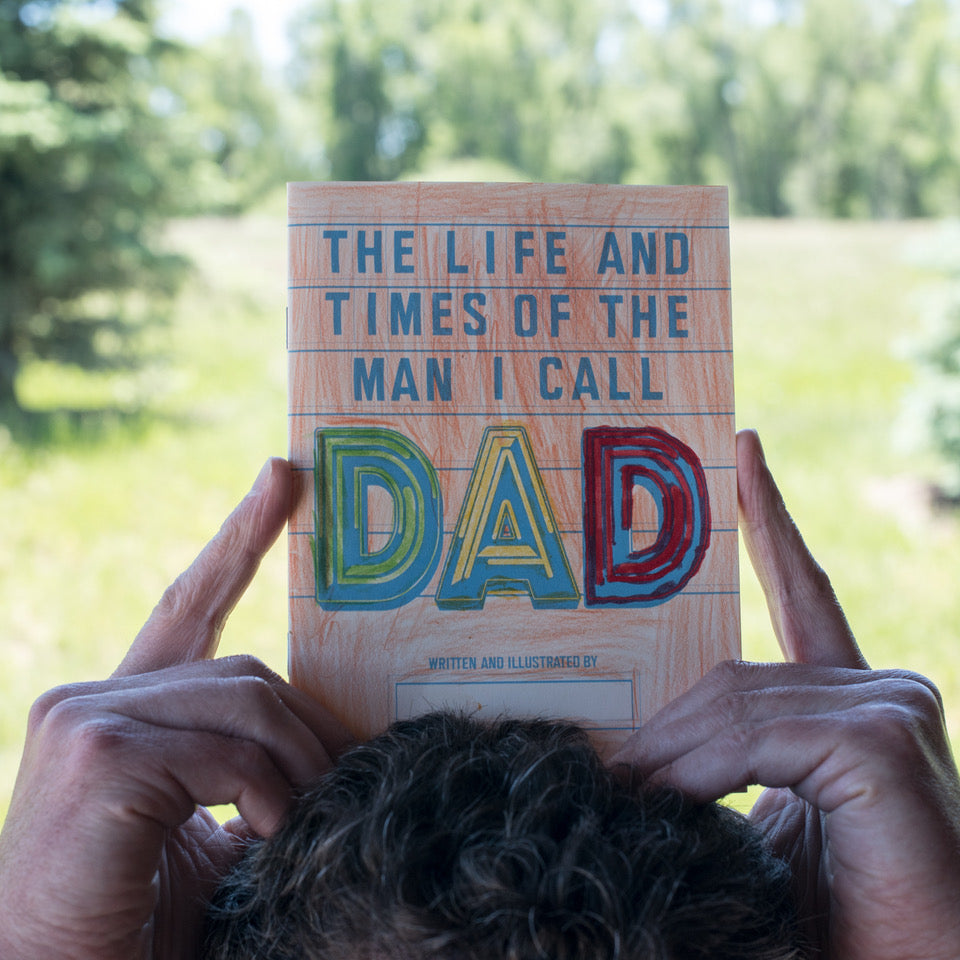 Book titled 'The Life and Times of the Man I Call Dad' held by a person with a blurred natural background