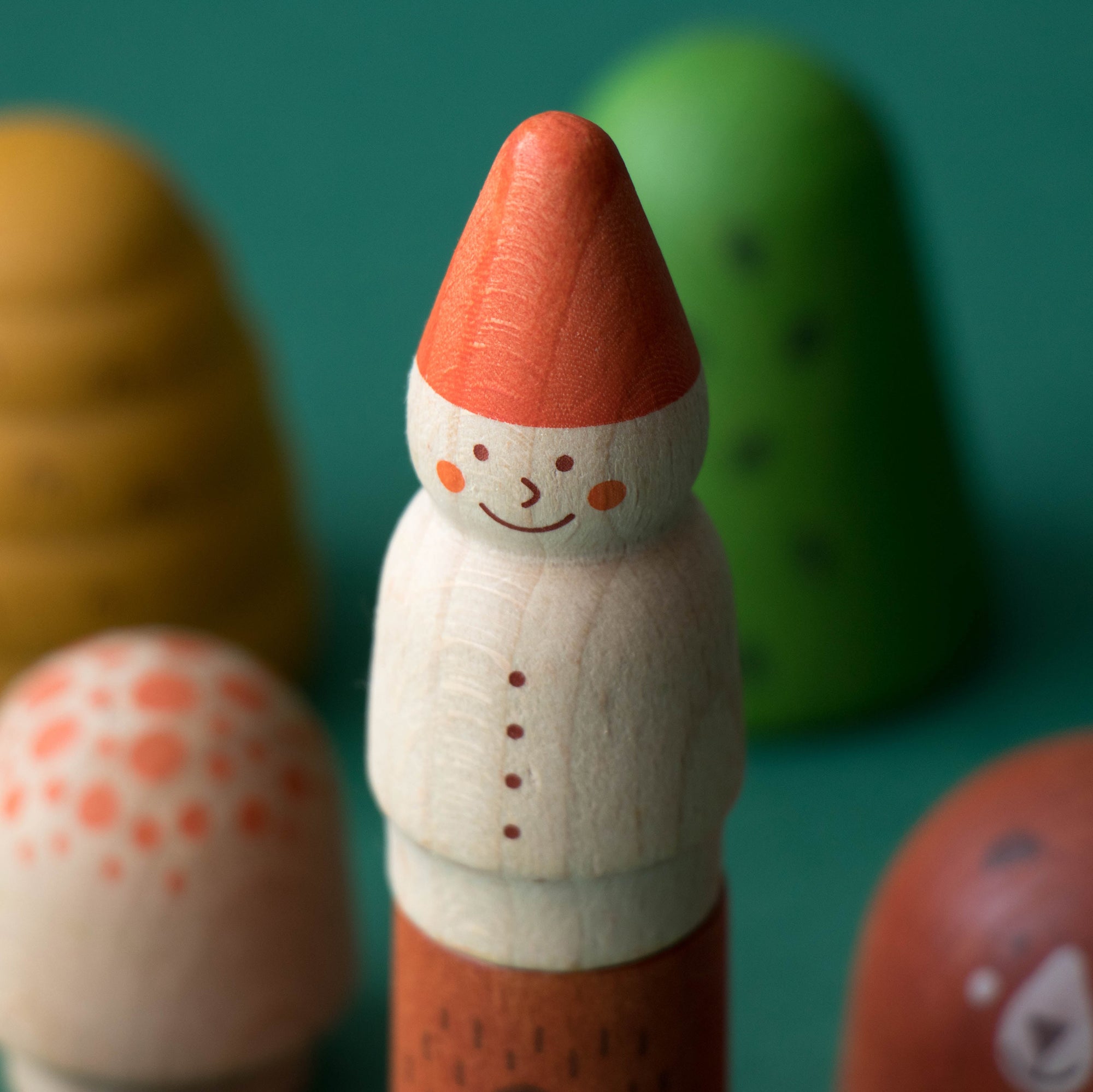 Wooden toy figure with a red hat and white face on a teal background