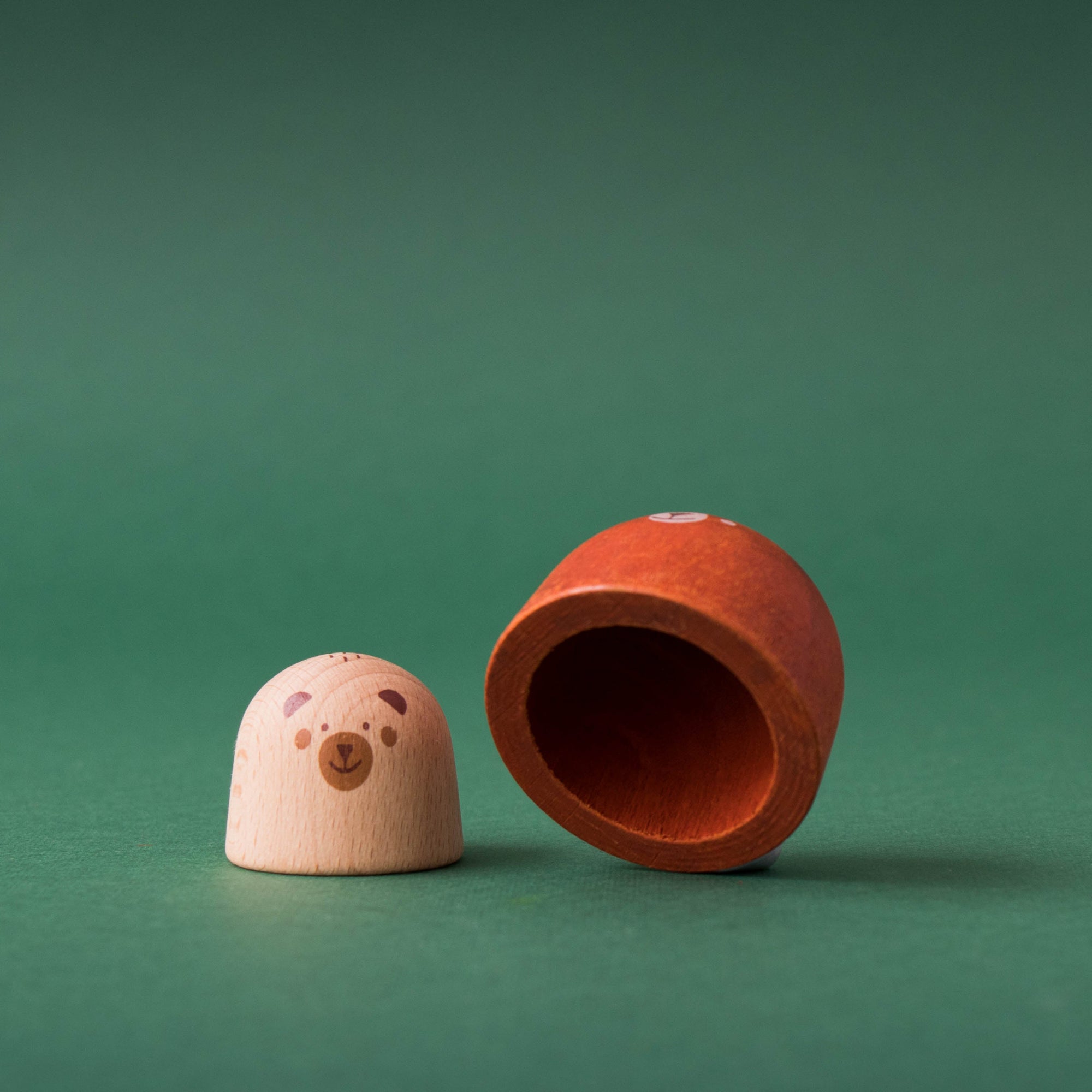 Two wooden toys, one resembling a bear and the other a smaller bear, on a green background.