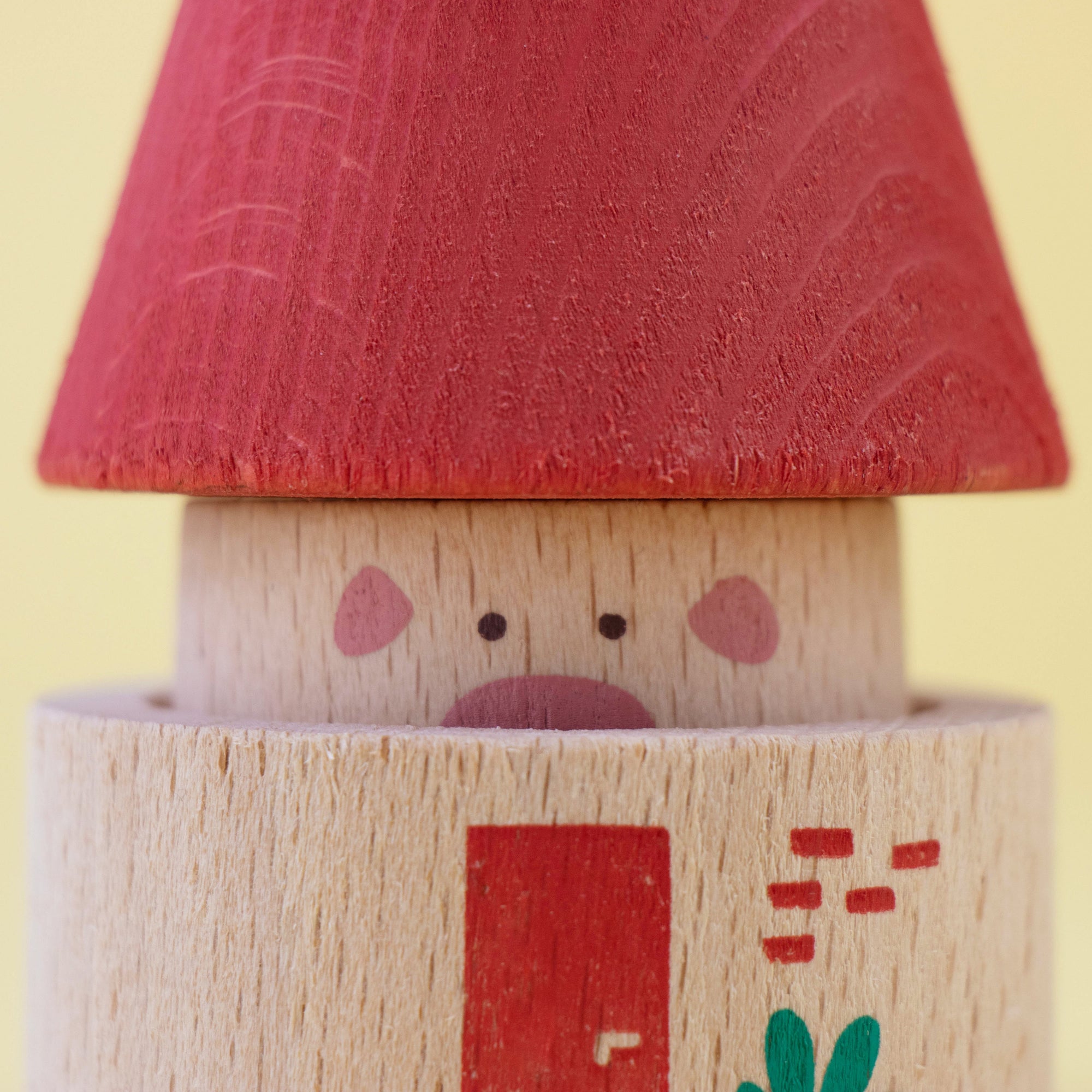 Wooden toy figure with a red hat and face on a yellow background