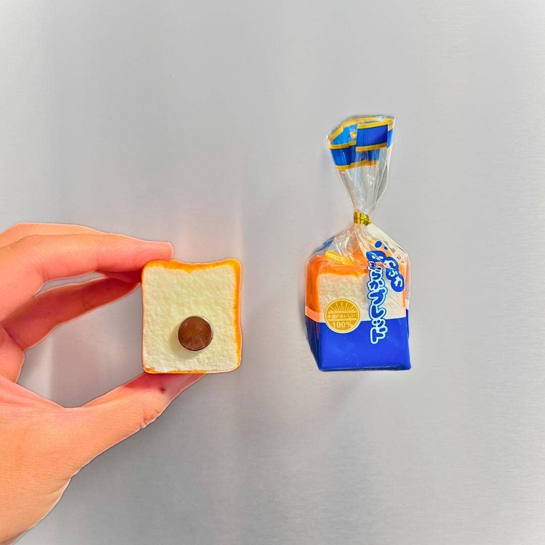 Miniature bread with a chocolate ball on a piece of bread, held by a hand next to its packaging.