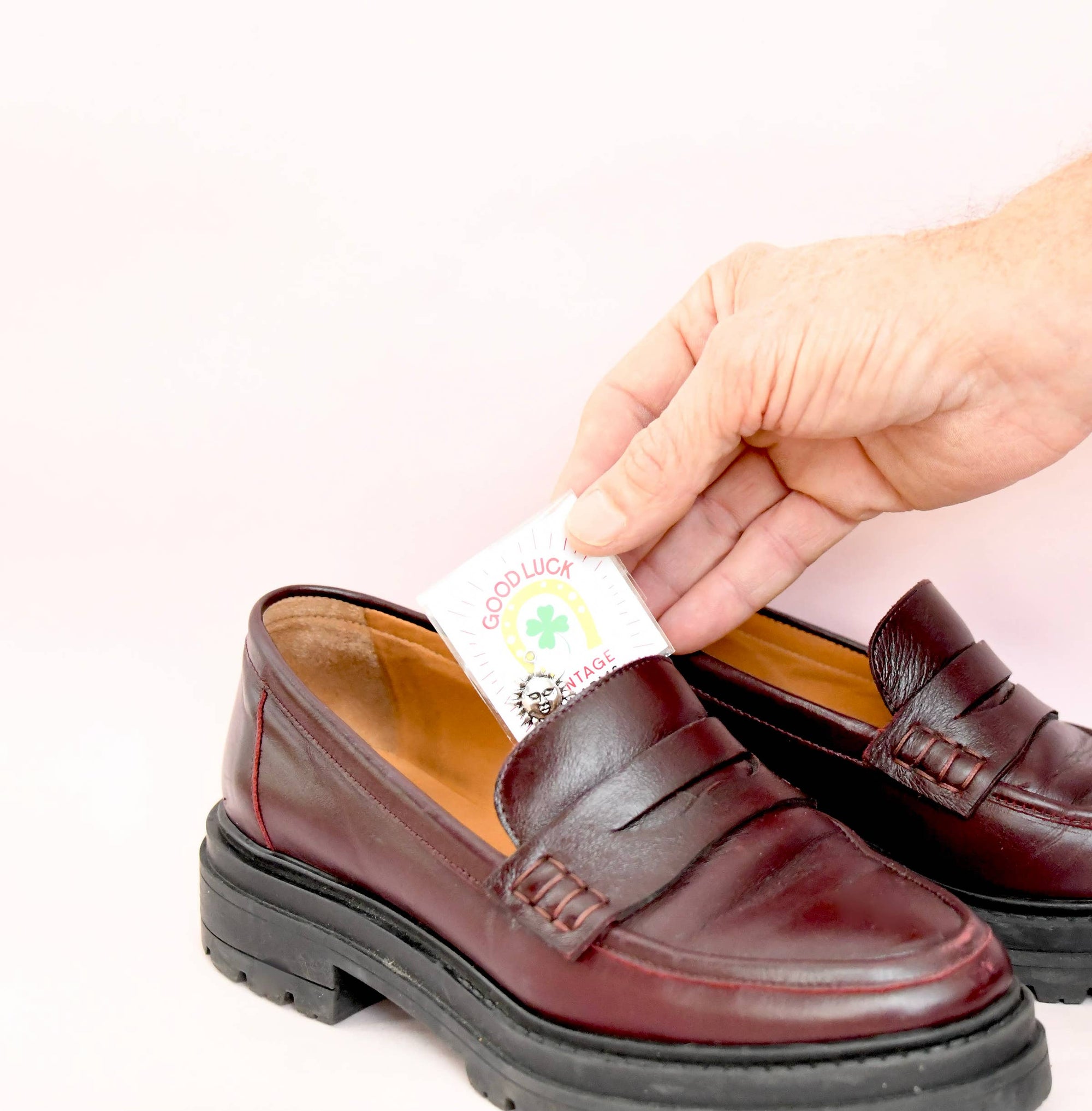 Brown leather shoe with a hand applying a white label featuring a rainbow and shamrock design.