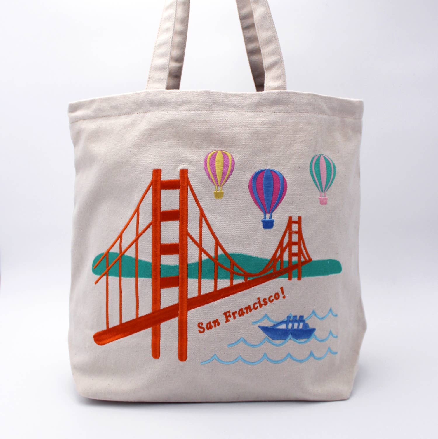 Tote bag with a design of the Golden Gate Bridge, hot air balloons, and a boat on a white background