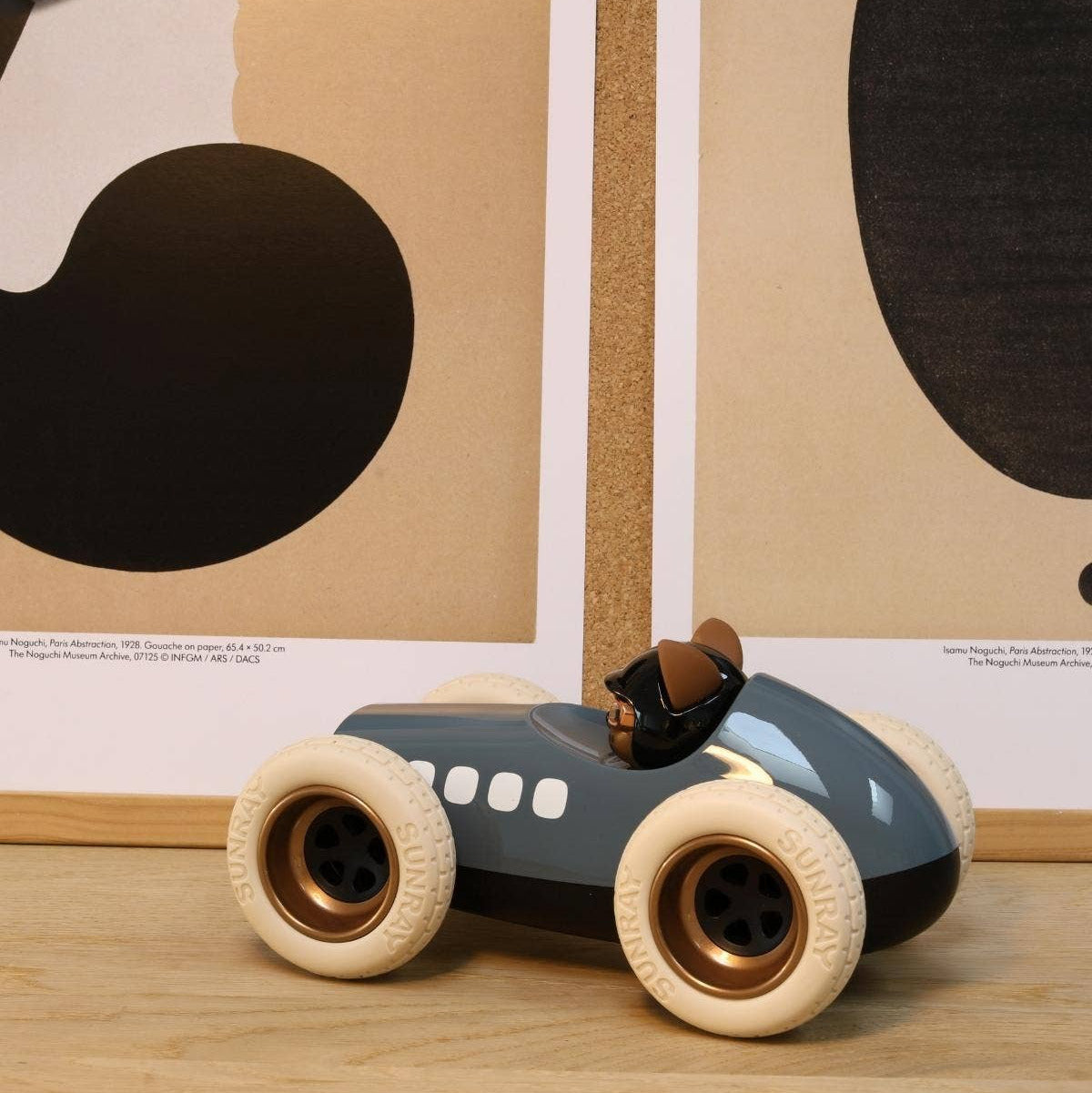 Toy car with a driver figure on a wooden surface with abstract wall art in the background