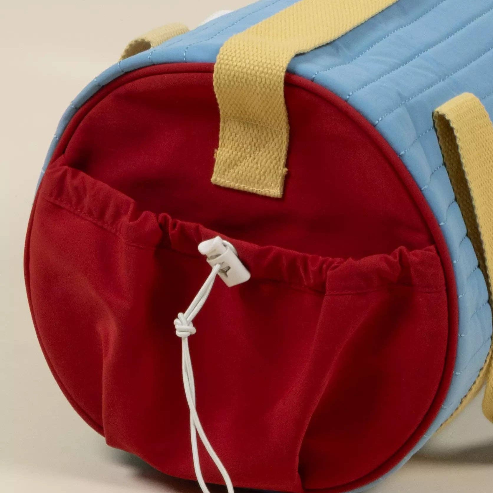 Red and blue duffel bag with yellow strap on a beige background