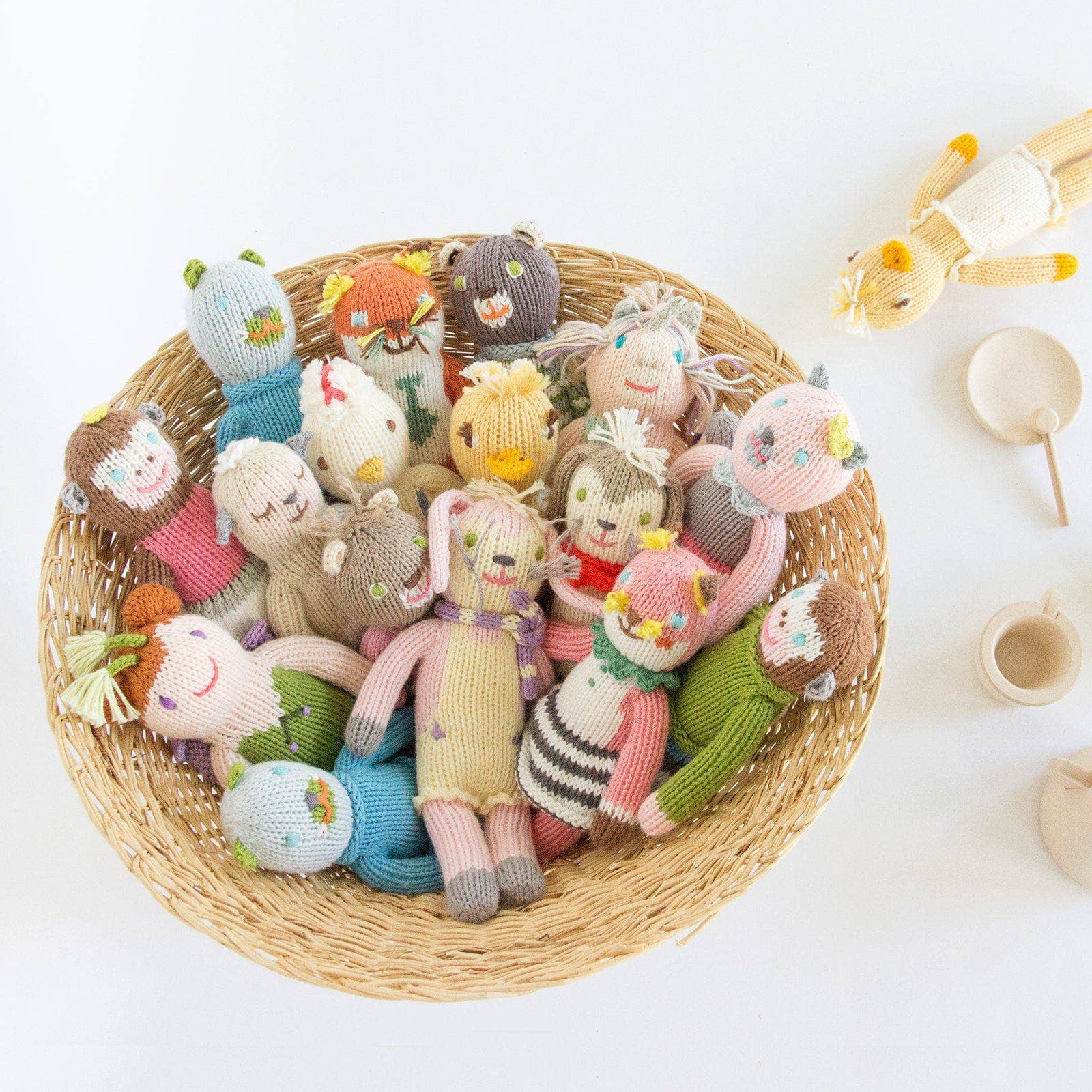 Wicker basket filled with colorful knitted dolls on a white background