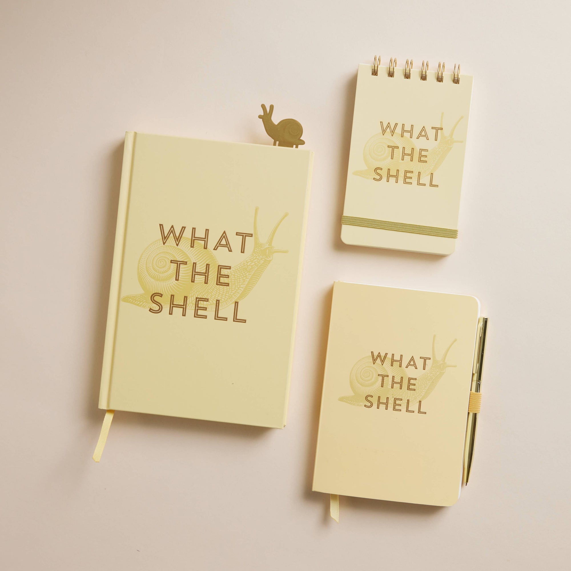 Three light yellow notebooks with 'What The Shell' text on a beige background